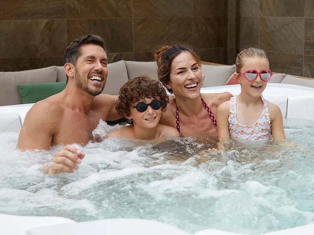 Family of four with parents and two children relaxing together in a hot tub